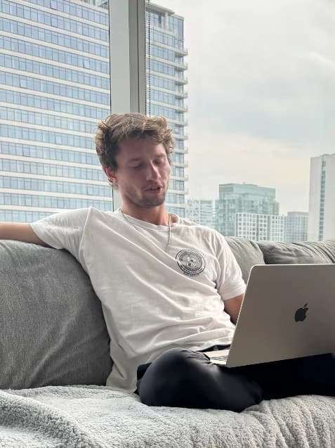 Rad Fugiel on the couch with his laptop, the city skyline behind him